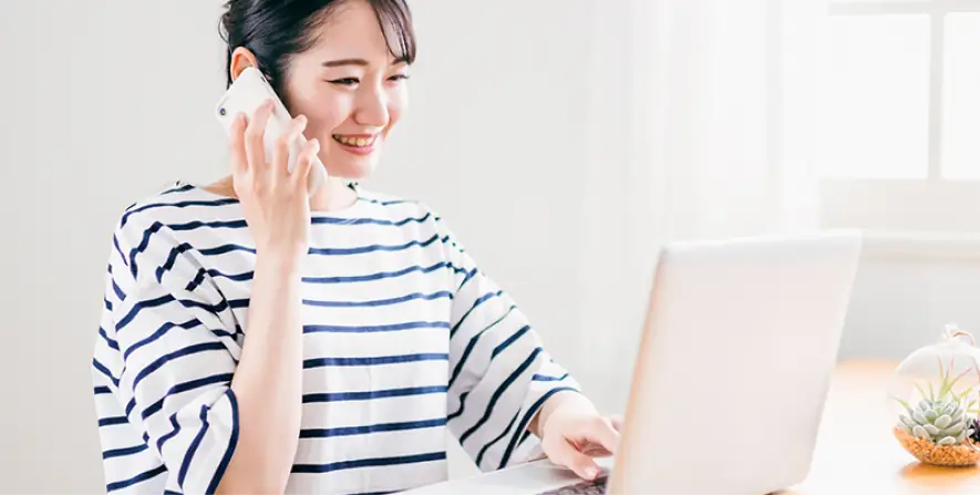 電話をしながらノートパソコンを操作する女性